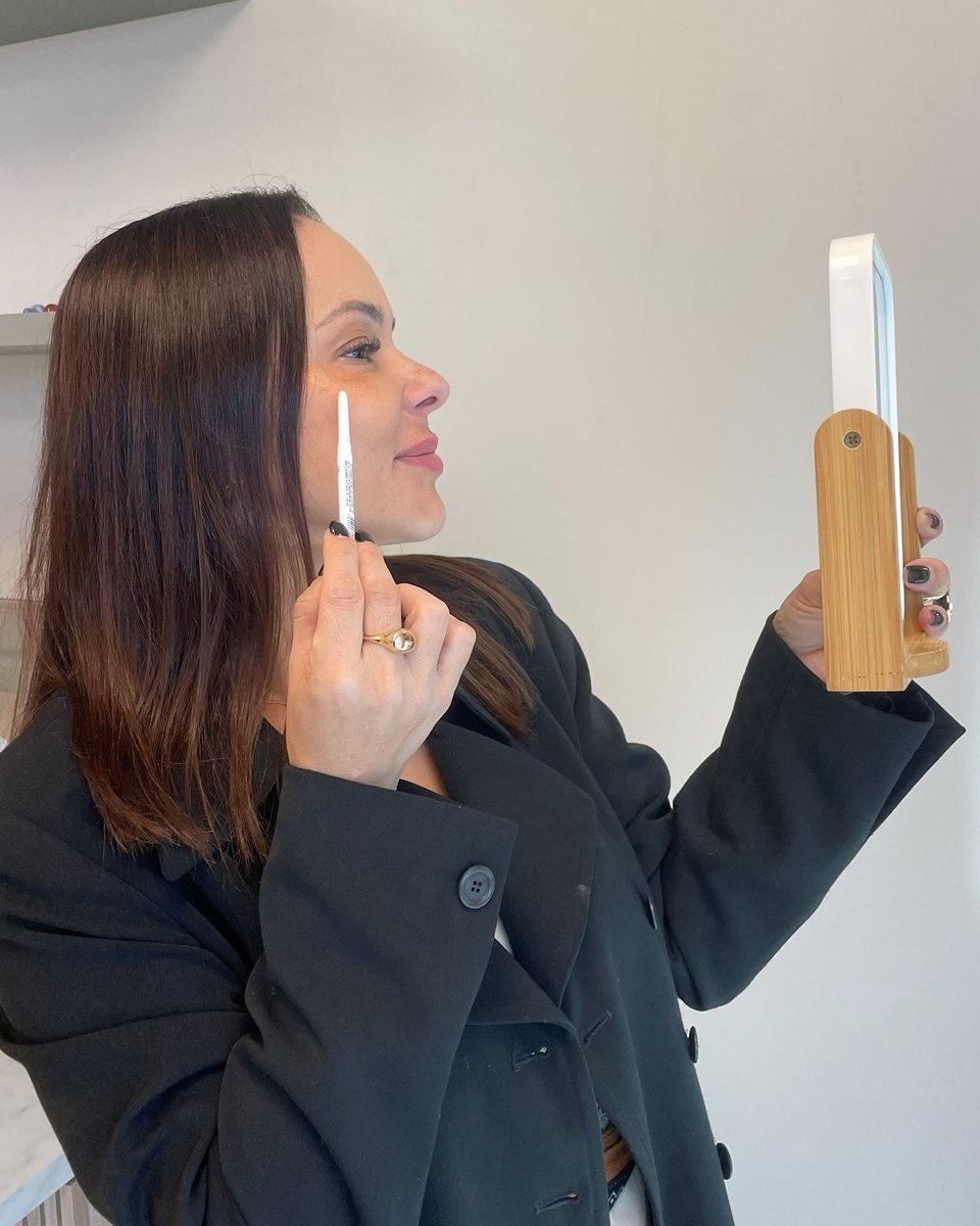 Dra. Ana Paula Neves marcando o próprio rosto com um lápis enquanto se olha no espelho